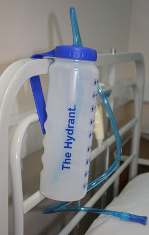 Hydrant bottle in clear plastic and long blue straw attached to a bedframe